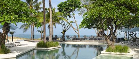 Zona de piscina con sillas de descanso y palmeras, con vistas al océano.