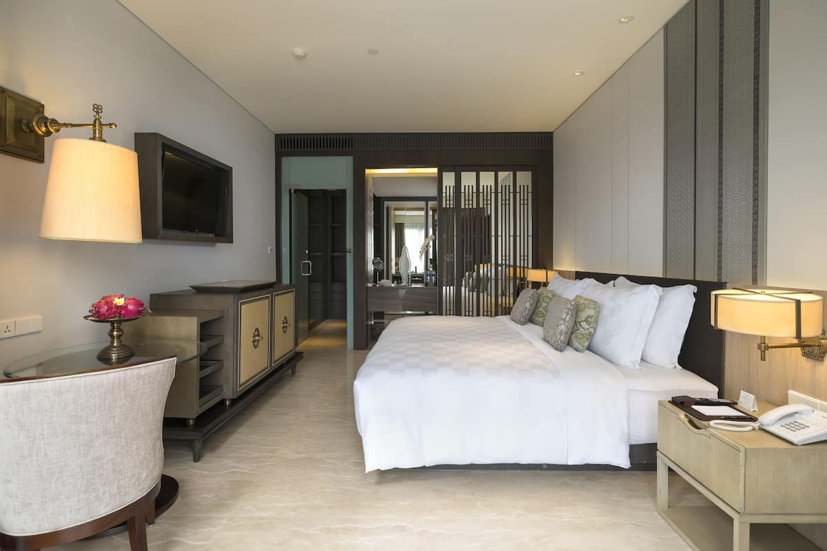 A modern hotel room with a large bed, bedside table, lamp, and a TV mounted on the wall.