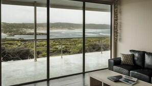 A modern living room with a large glass door leading to a balcony overlooking a coastal landscape.