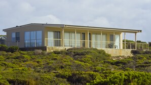 A modern two-story building with large windows and a balcony, surrounded by dense green vegetation.