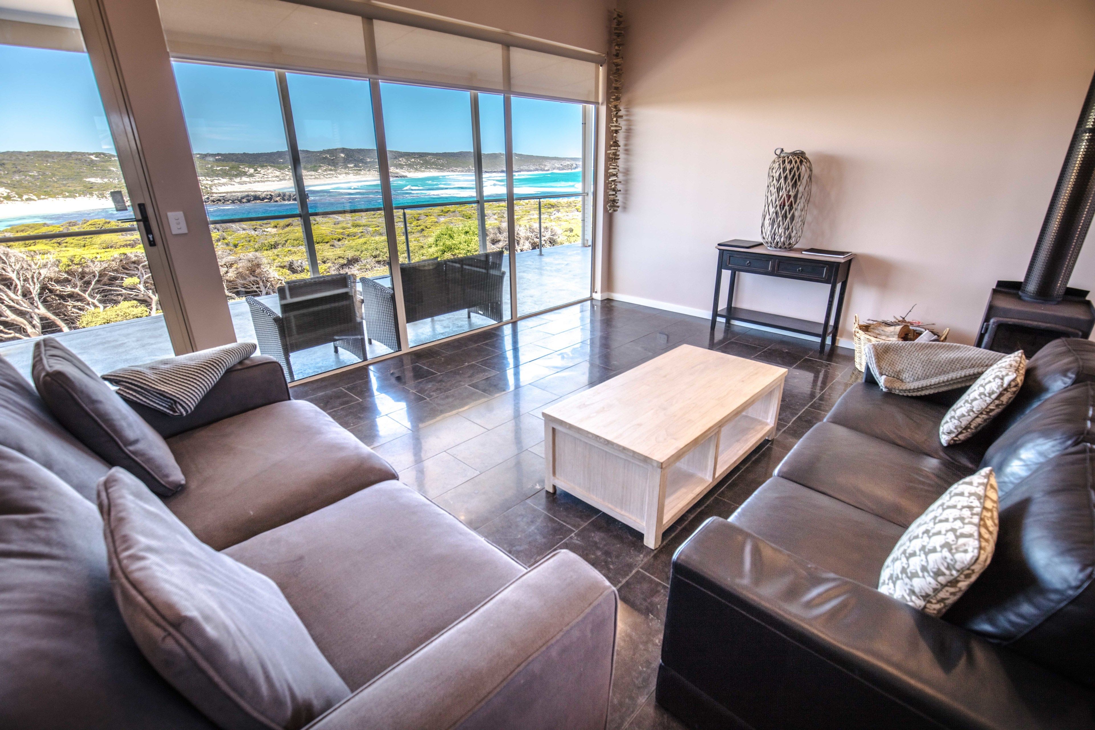 A modern living room with a large glass door leading to a balcony with a view of the ocean.