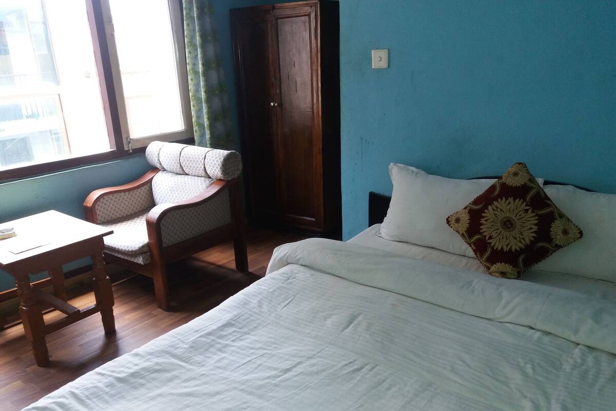 A room with a bed, a wooden chair, a small table, and a window with curtains.