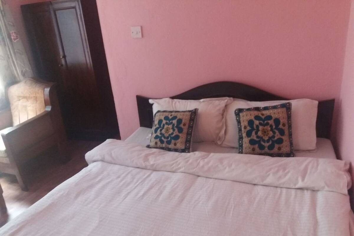 A bed with white bedding and two decorative pillows, a wooden headboard, and a pink wall.