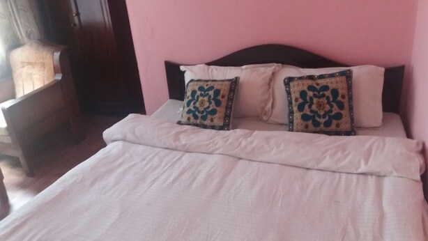 Una cama con ropa blanca, dos almohadas decorativas, un cabecero de madera y una pared rosa.