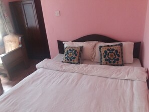 A bed with white bedding and two decorative pillows, a wooden headboard, and a pink wall. - King's Land Hotel (Kathmandu)