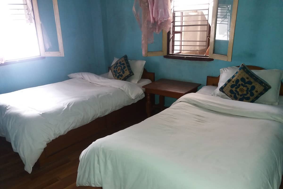 A room with two beds, a wooden table, and a window with a metal grill.