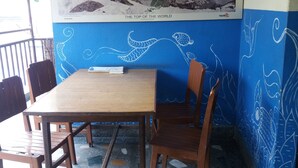 Un comedor con una mesa y sillas, un cartel con una cadena montañosa, y una pared azul con diseños blancos.