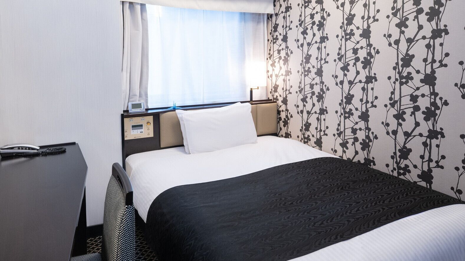 A hotel room with a bed, bedside table, and a window with curtains.