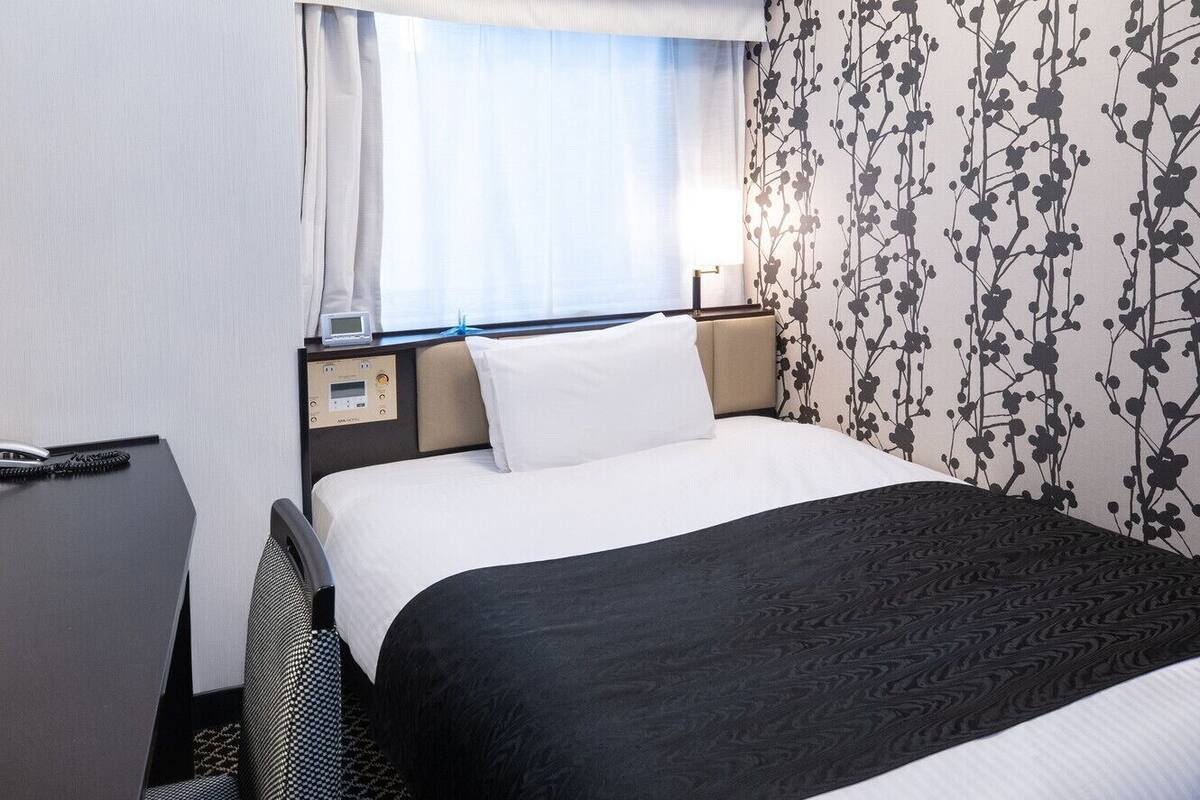 A hotel room with a bed, bedside table, and a window with curtains.