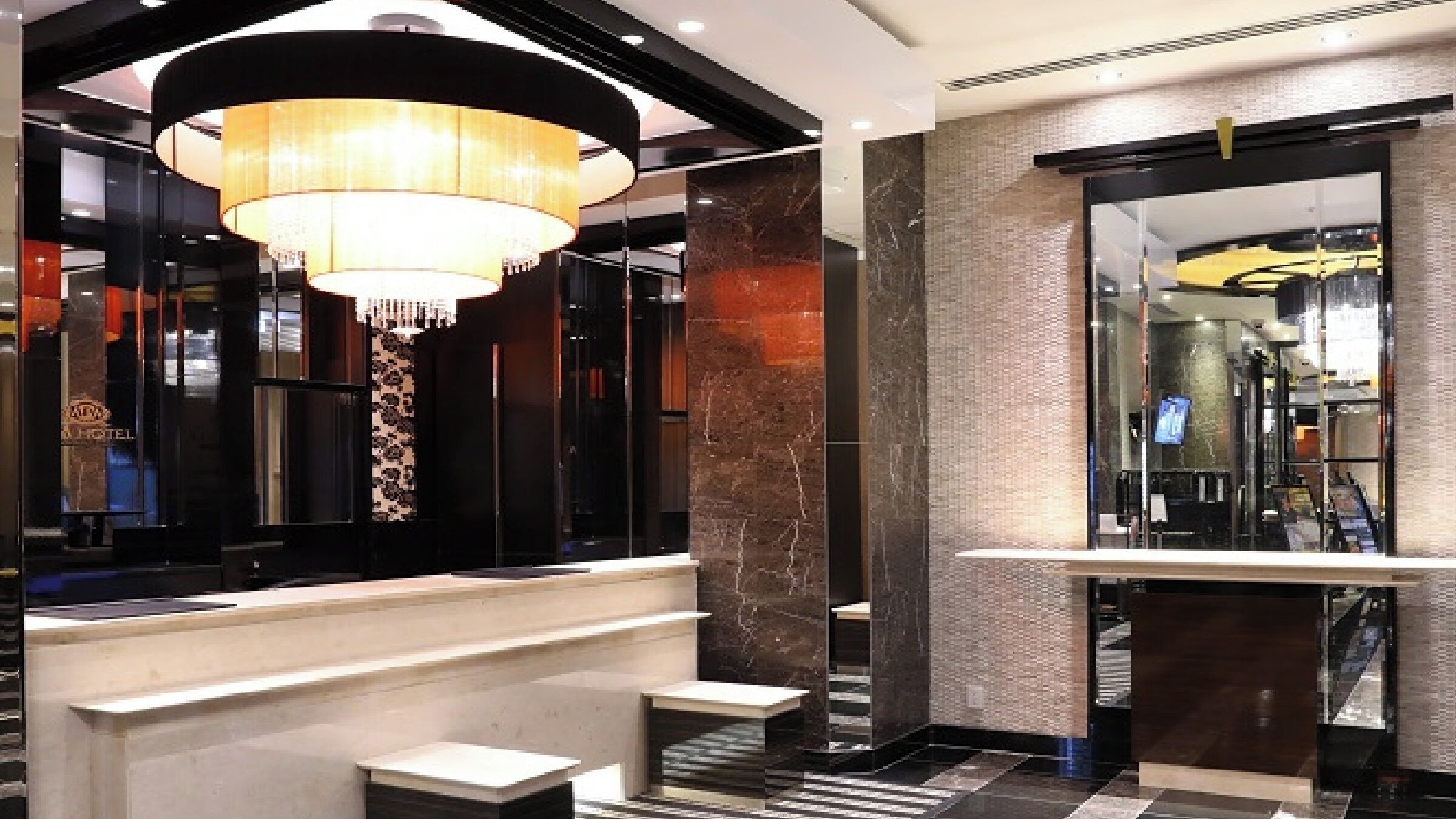Um saguão de hotel moderno, com um lustre imponente, colunas de mármore e uma recepção.
