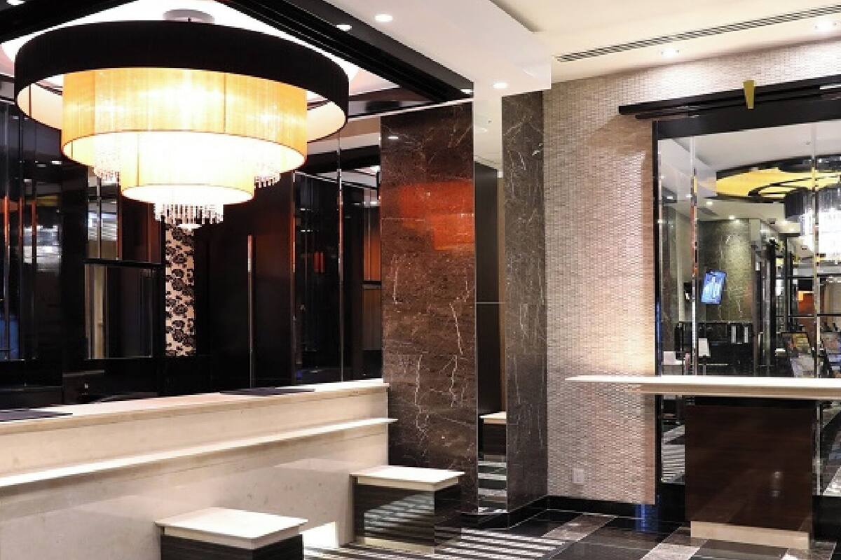 A modern hotel lobby with a grand chandelier, marble columns, and a reception desk.