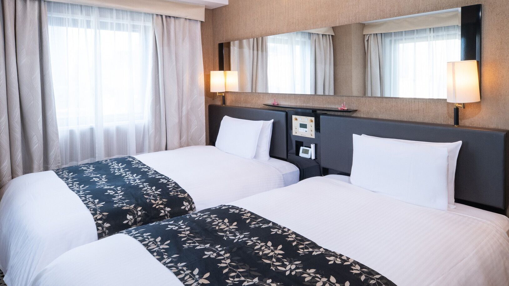 A hotel room with two beds, a large mirror, and a control panel on the headboard.