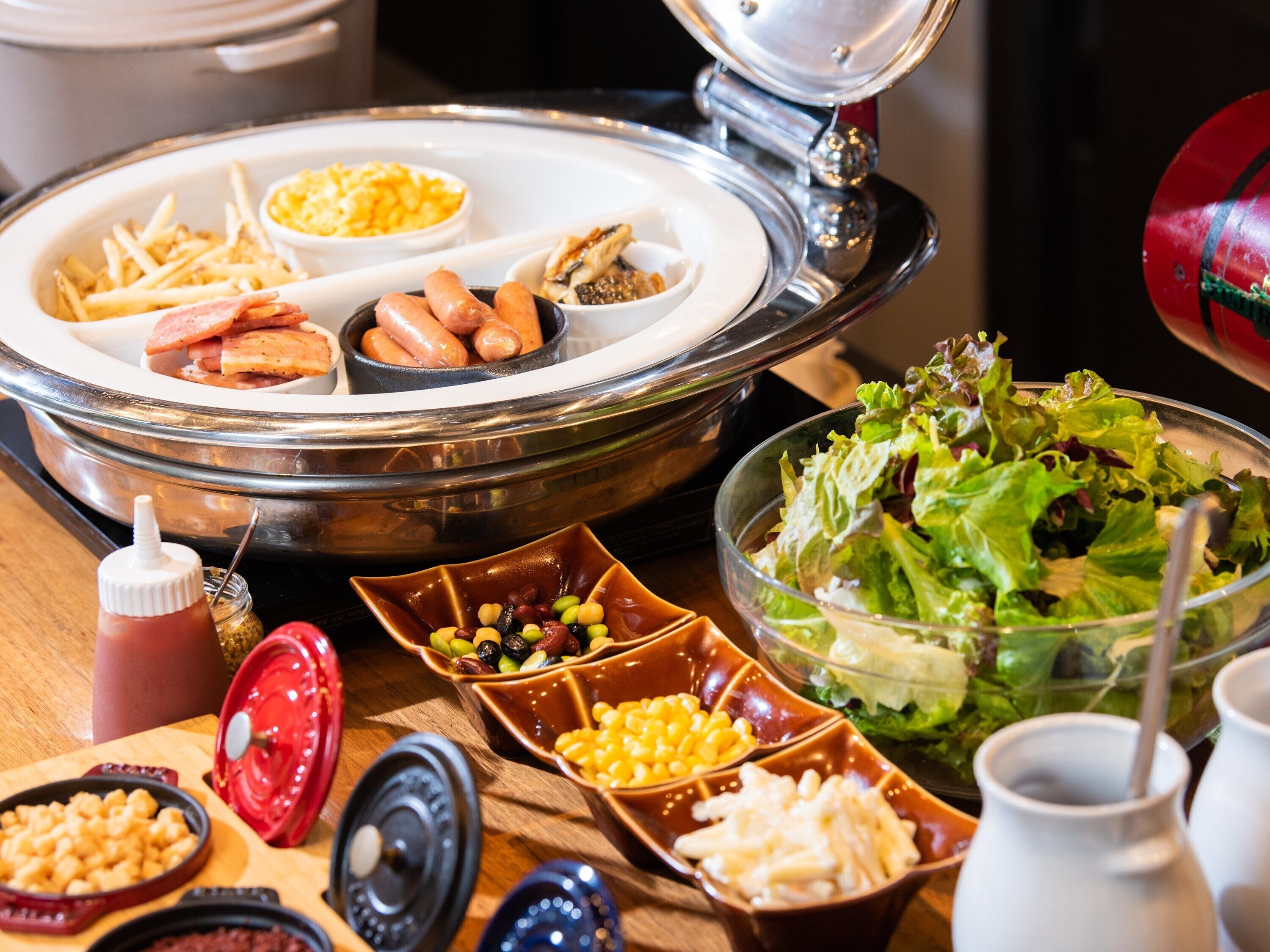 Une table de buffet proposant divers plats, notamment des salades, des macaronis et des saucisses.
