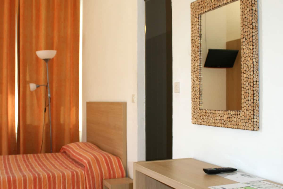 Una habitación de hotel con cama, escritorio, silla, lámpara y espejo.