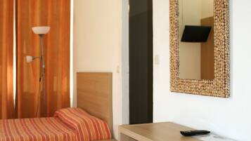 Quarto de hotel com cama, escrivaninha, cadeira, abajur e espelho.