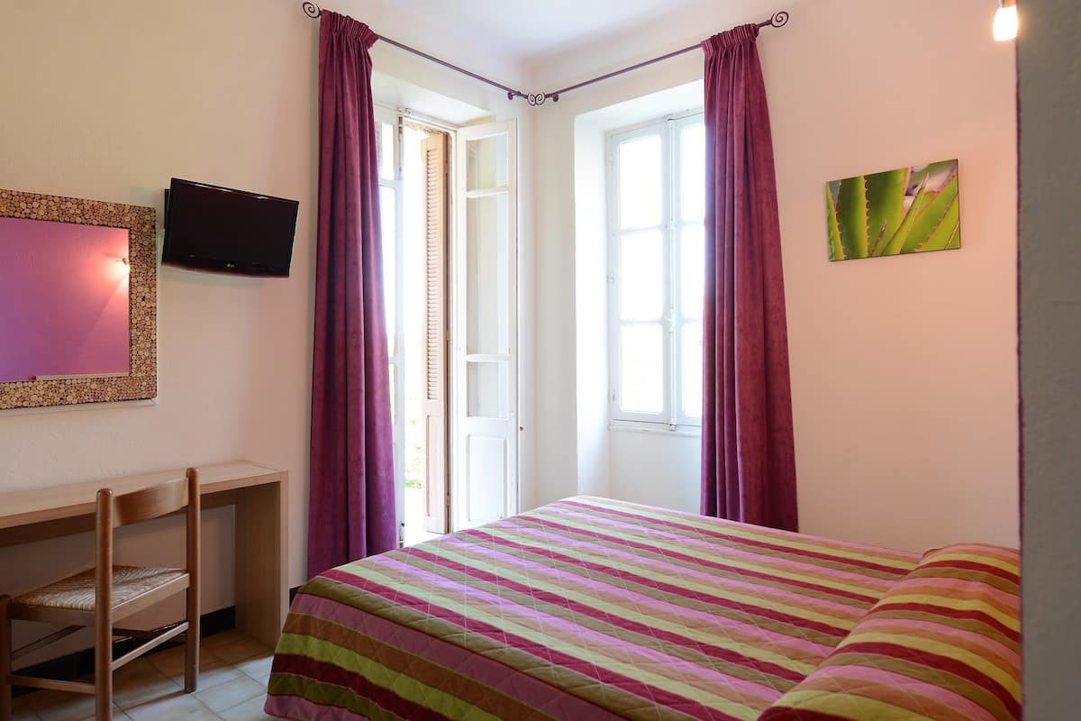 Un dormitorio con cama, escritorio, silla, televisor y ventana con cortinas.