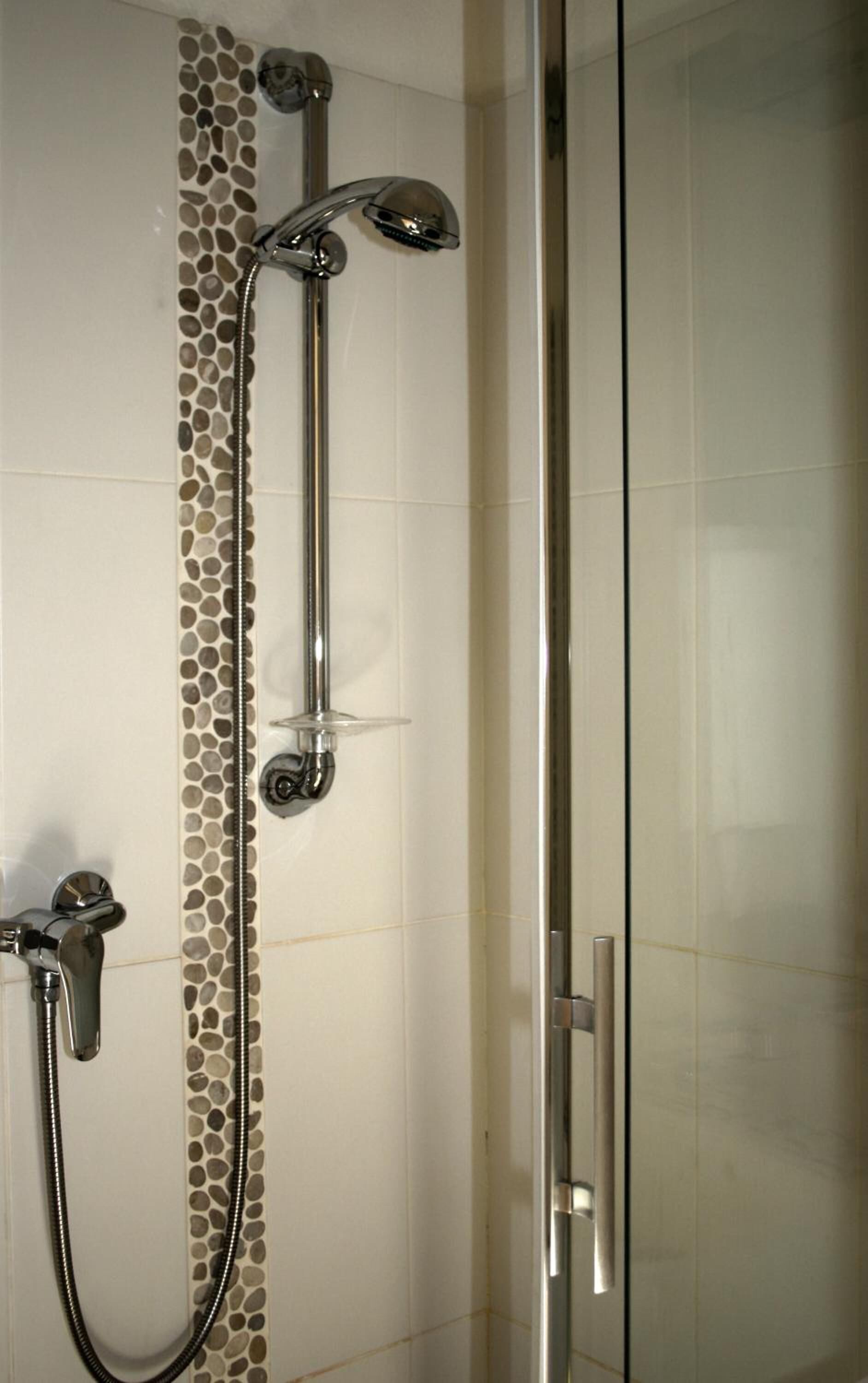 A shower with a glass door and a tiled wall with a pebble pattern.