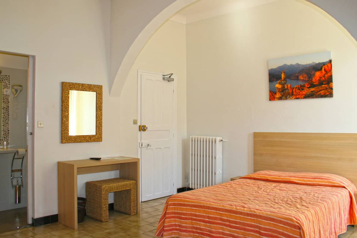 Un dormitorio con cama, escritorio, silla, espejo y un cuadro en la pared.