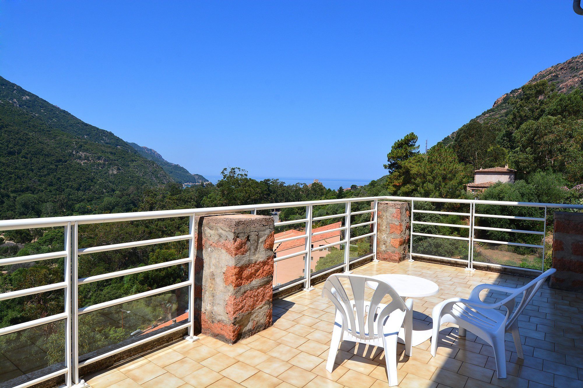 A balcony with a view of the sea, white plastic chairs, and a tiled floor.