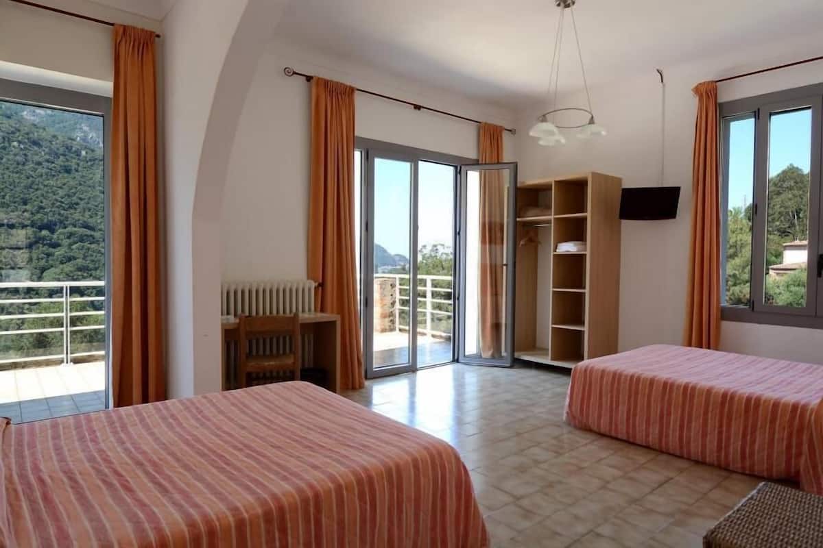 Habitación de hotel con dos camas, televisión, armario y balcón con vistas a las montañas.