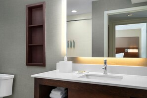 Un baño moderno con un lavamanos blanco, un espejo y un estante de madera.