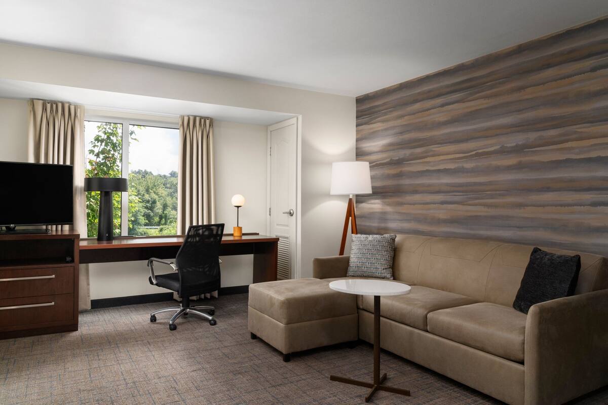 Ein Hotelzimmer mit Schreibtisch, Fernseher, Sofa und Lampe.