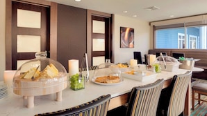 Montaje de un bufé de desayuno con diversas opciones de comida, como pan, cereales y frutas, en un comedor moderno de hotel con sillas a rayas y un ventanal grande.