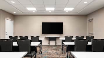 A conference room with a large flat-screen TV, multiple tables, and chairs arranged for meetings.