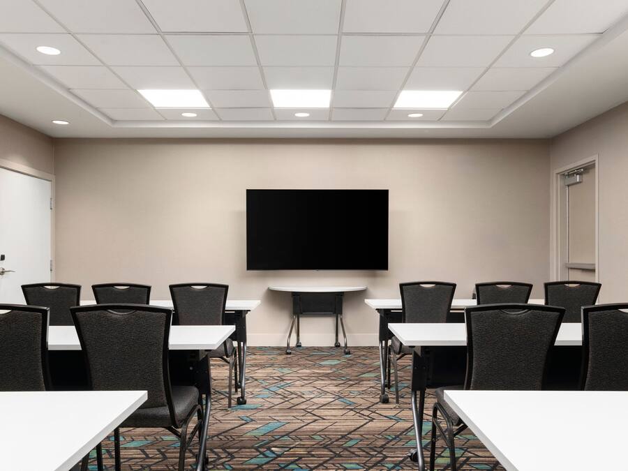 A conference room with a large flat-screen TV, multiple tables, and chairs arranged for meetings.