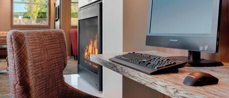 A modern hotel room with a fireplace, a desk with a Lenovo monitor, keyboard, and mouse.