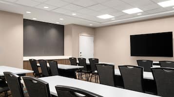 A conference room with tables and chairs, a projector screen, and a flat-screen TV.