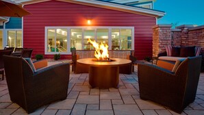 Un patio al aire libre con un brasero, muebles de mimbre y un edificio rojo al fondo.