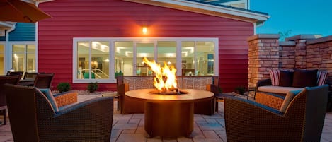 Eine Terrassenausstattung im Freien mit einem Feuerkorb, Korbmöbeln und einem roten Gebäude im Hintergrund.