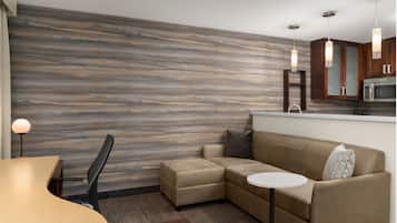 A modern hotel room with a wood-textured wall, a sofa, a small table, a chair, and a kitchenette area.