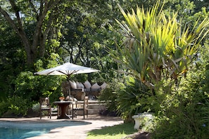 Uma área na piscina com um banco de pedra, uma mesa e um guarda-sol.