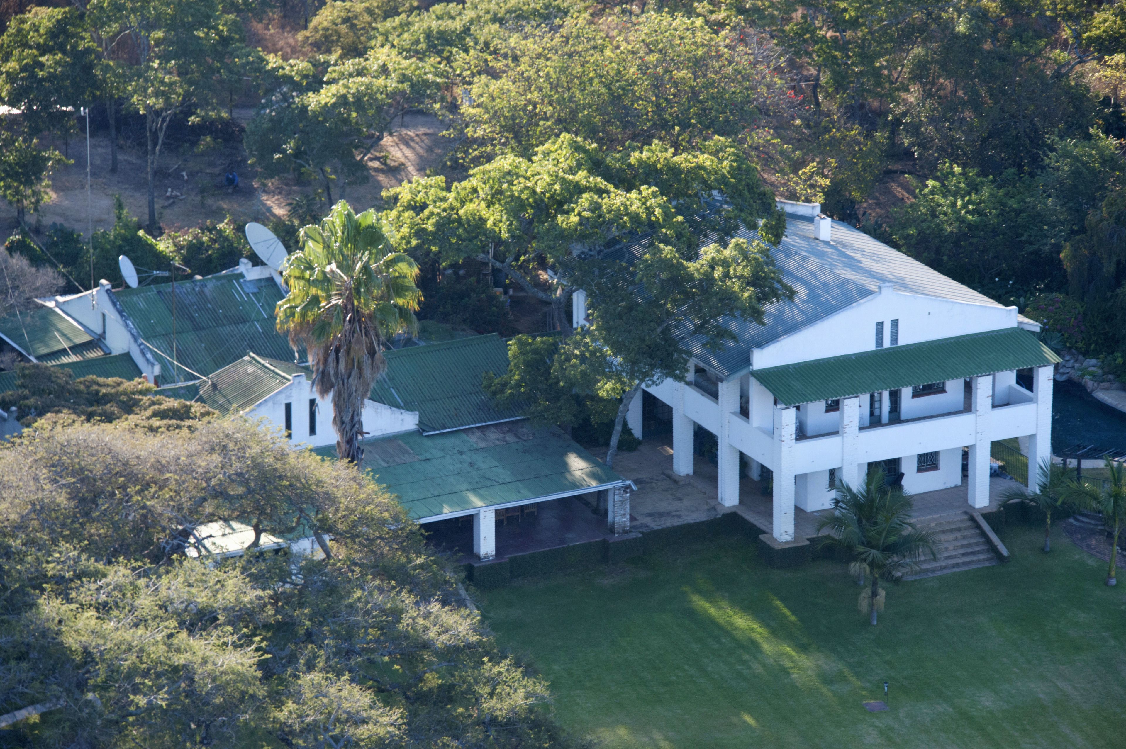 A large white building with a green roof, surrounded by lush greenery and trees.