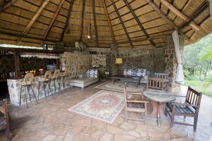 Un área de estar al aire libre de estilo rústico con muros de piedra, techo de paja y una barra con sillas de mimbre.