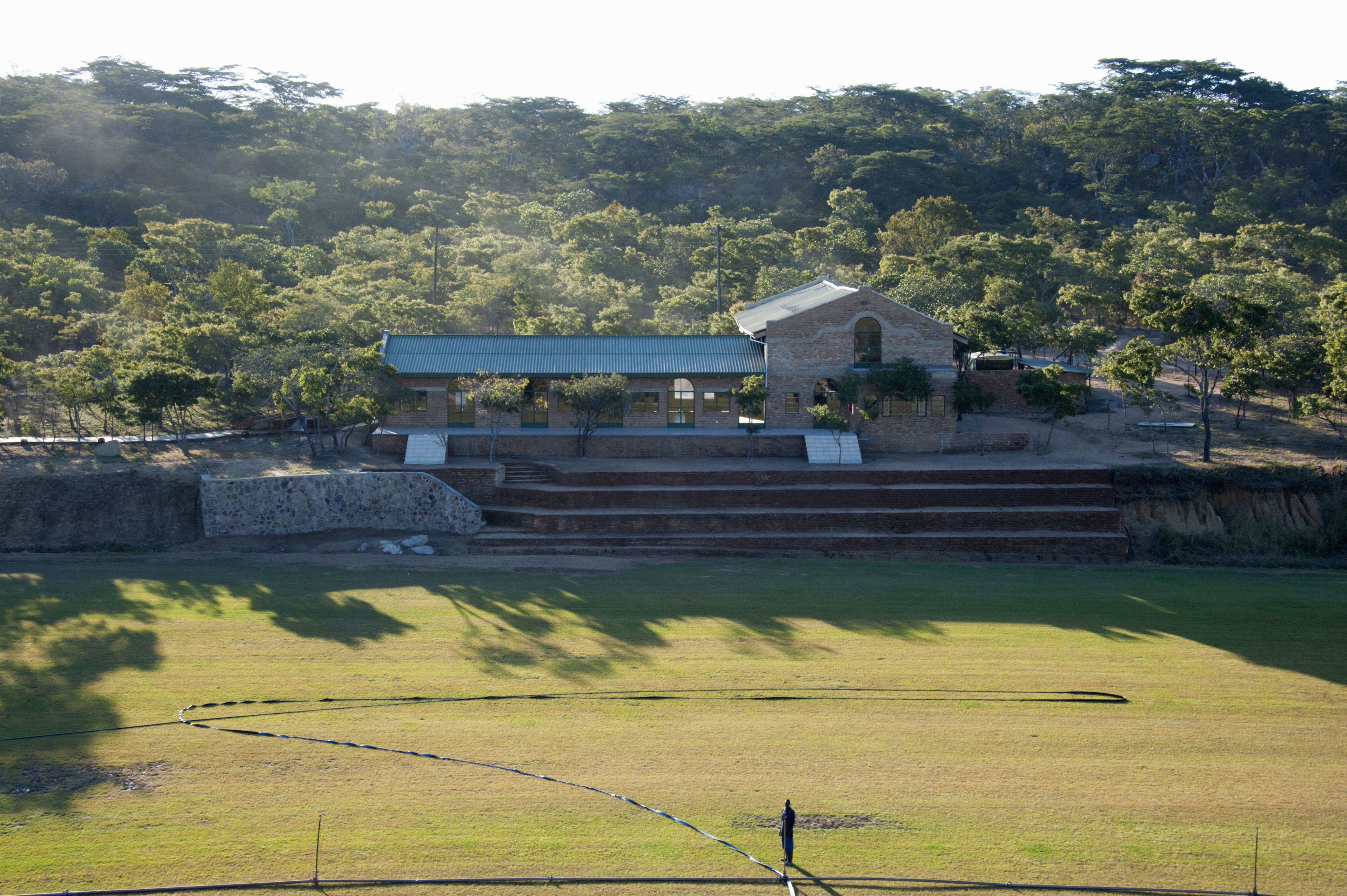 A building with a green roof and a brick structure, surrounded by a grassy area and trees.