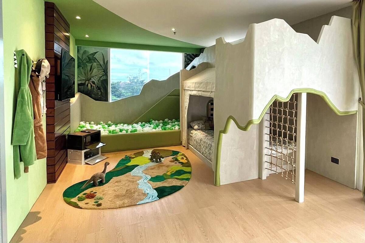Una habitación infantil con una cama litera, una piscina de bolas y un ventanal grande.