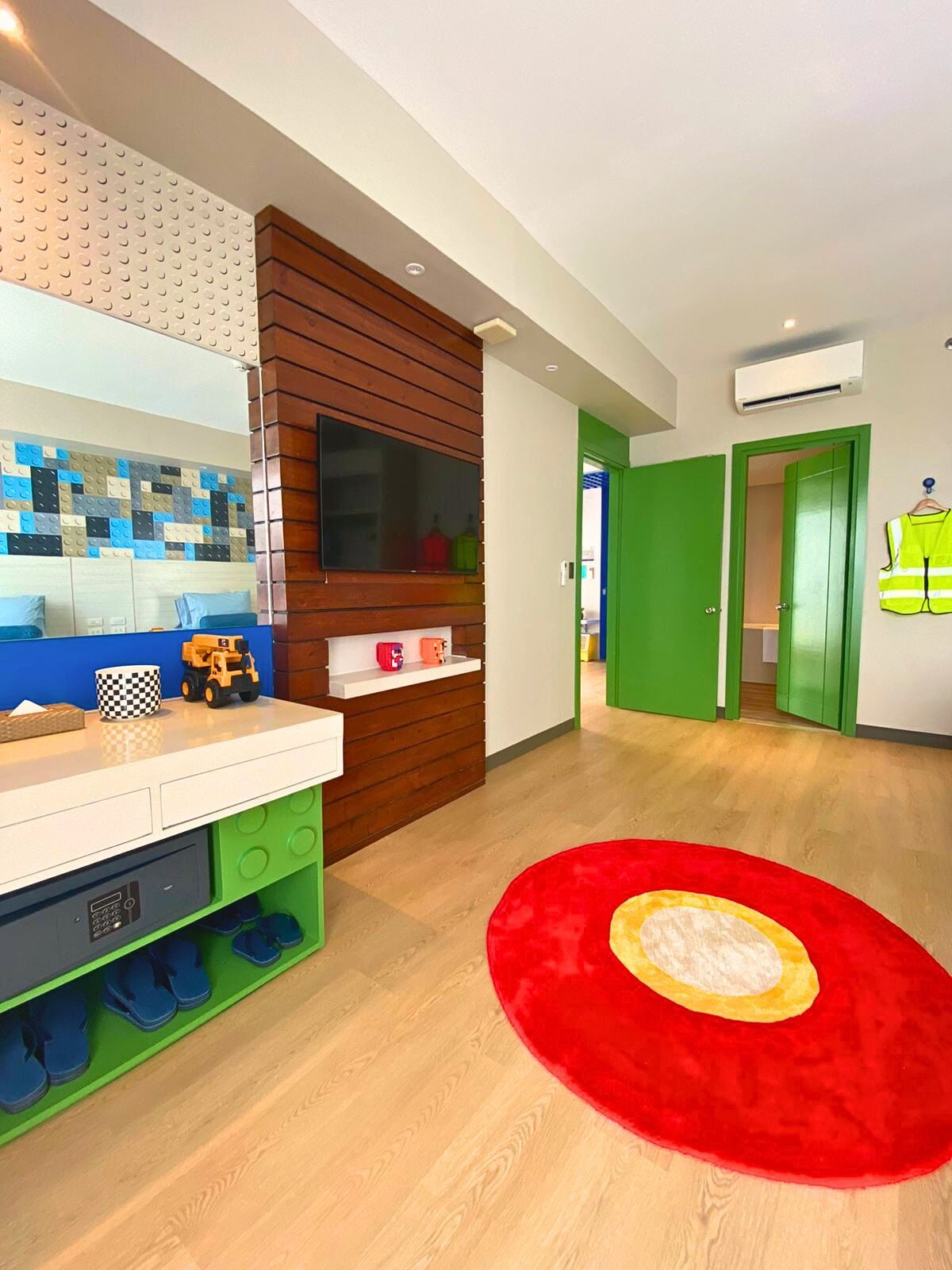 A room with a wooden vanity, a mirror, a red rug, and a green door.