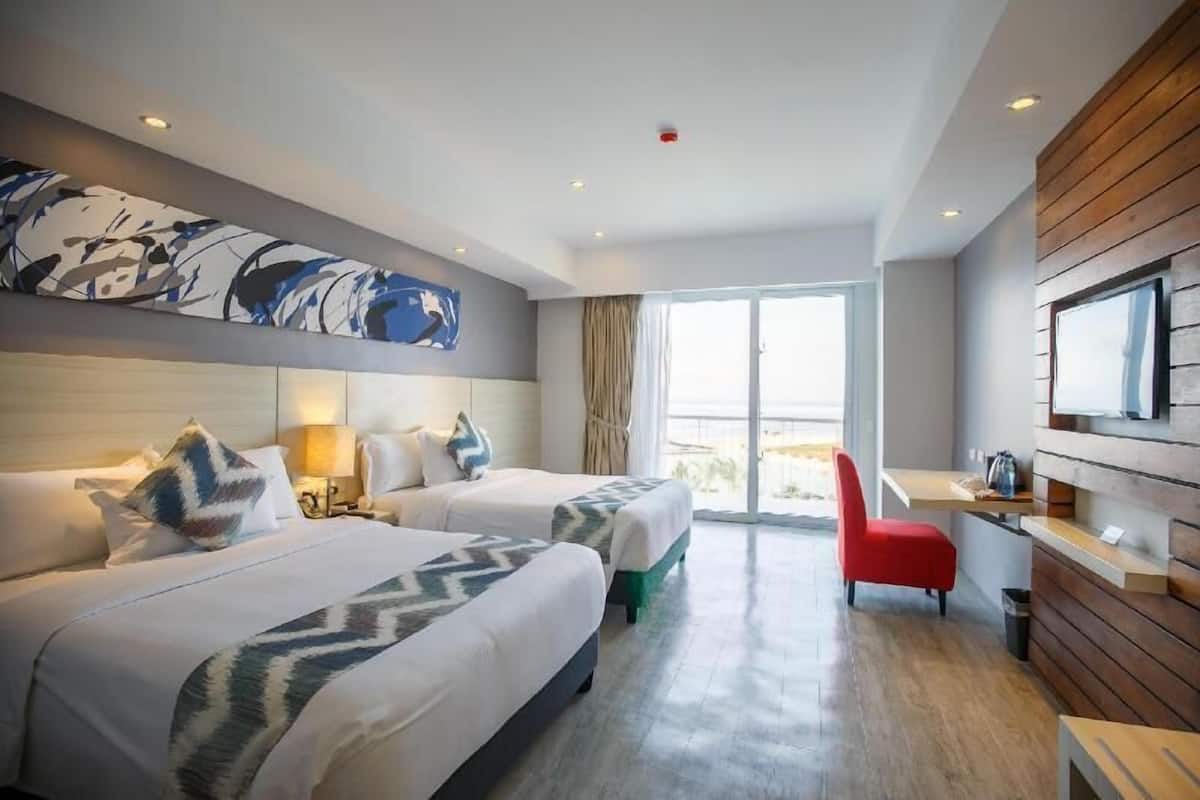 A hotel room with two beds, a desk, a chair, and a large window.