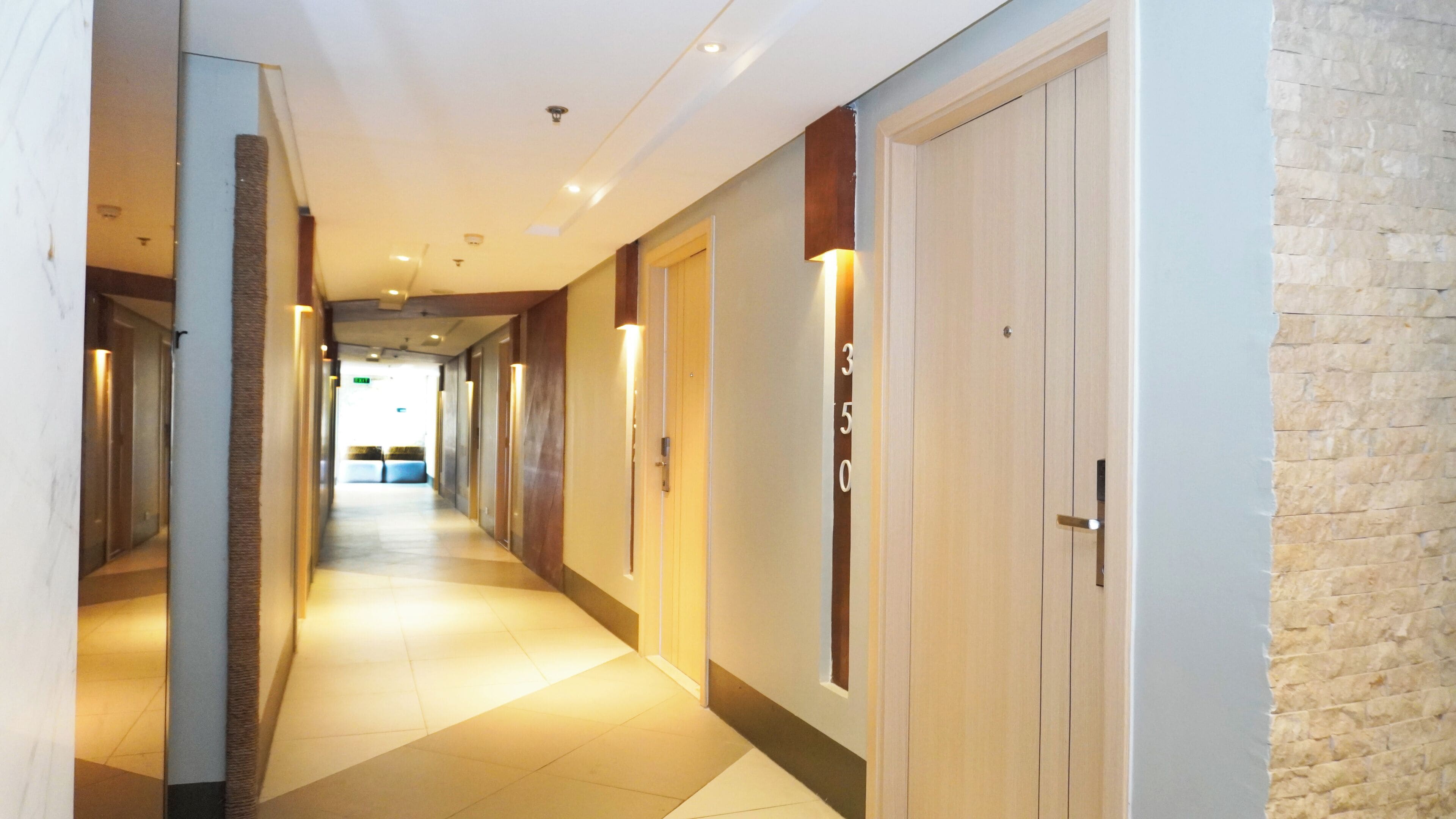 A hotel corridor with a tiled floor, wooden doors, and a brick wall on the right.