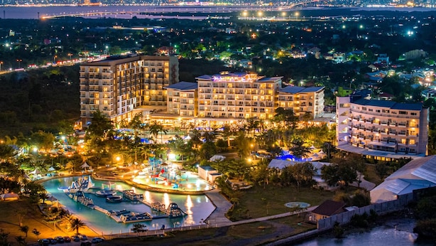 Un hotel con varias construcciones, una piscina y vista a un paisaje urbano de noche.