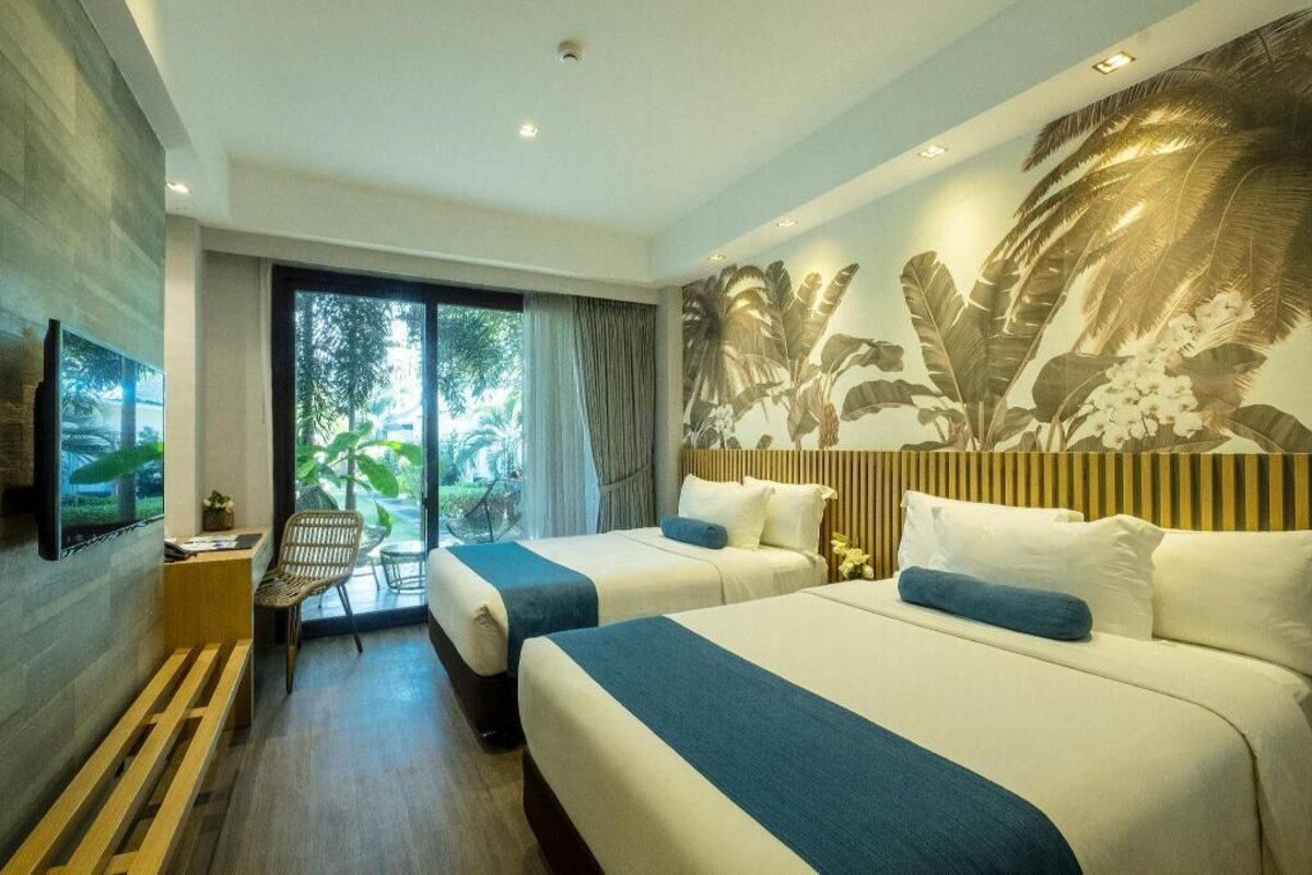 Habitación de hotel con dos camas, televisión, escritorio y vistas a zonas verdes.