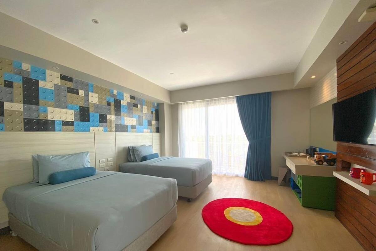 Habitación de hotel con dos camas, una alfombra roja, un televisor y una pared con diseño geométrico.