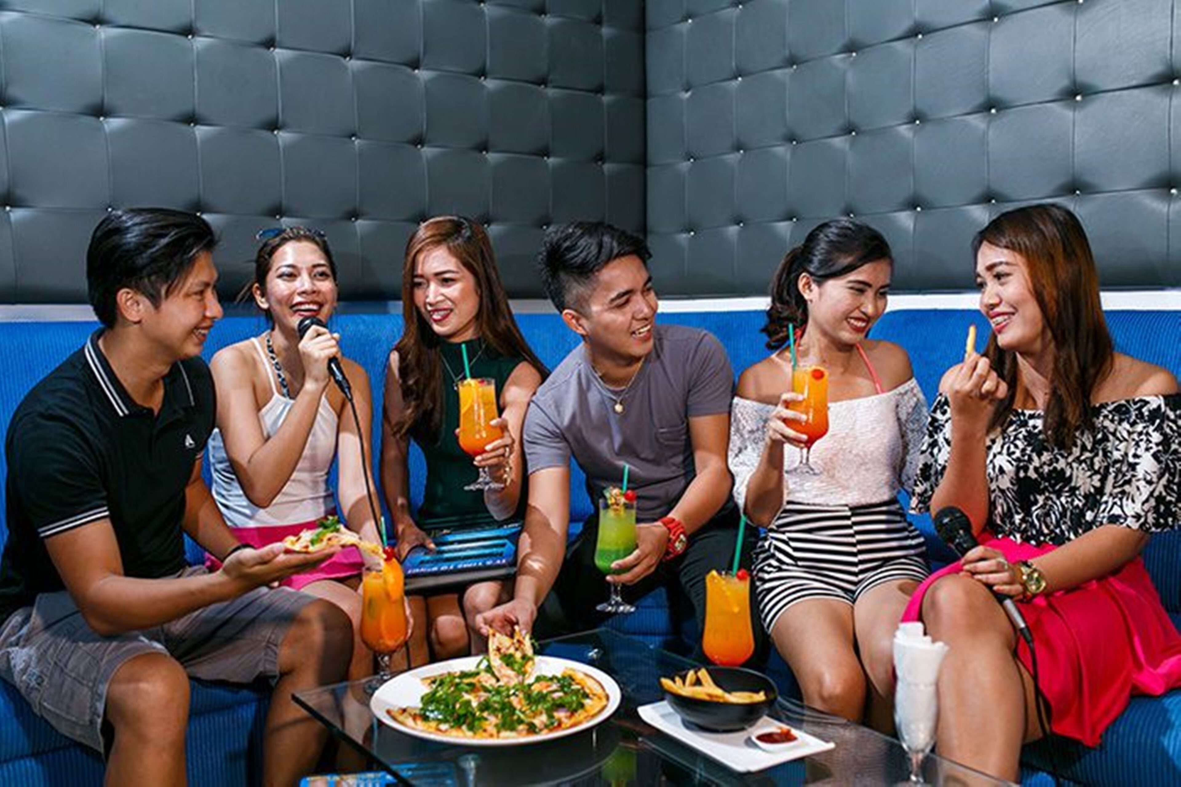 A group of people sitting on a blue couch in a room with a tufted headboard.