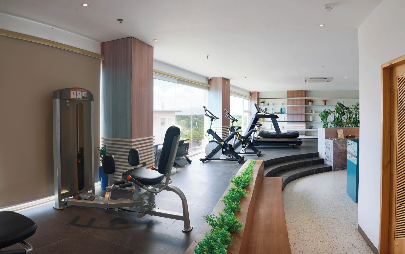 Ein modernes Fitnessstudio mit unterschiedlichen Trainingsgeräten, einer Treppe und einem Empfangs Bereich mit Pflanzen.