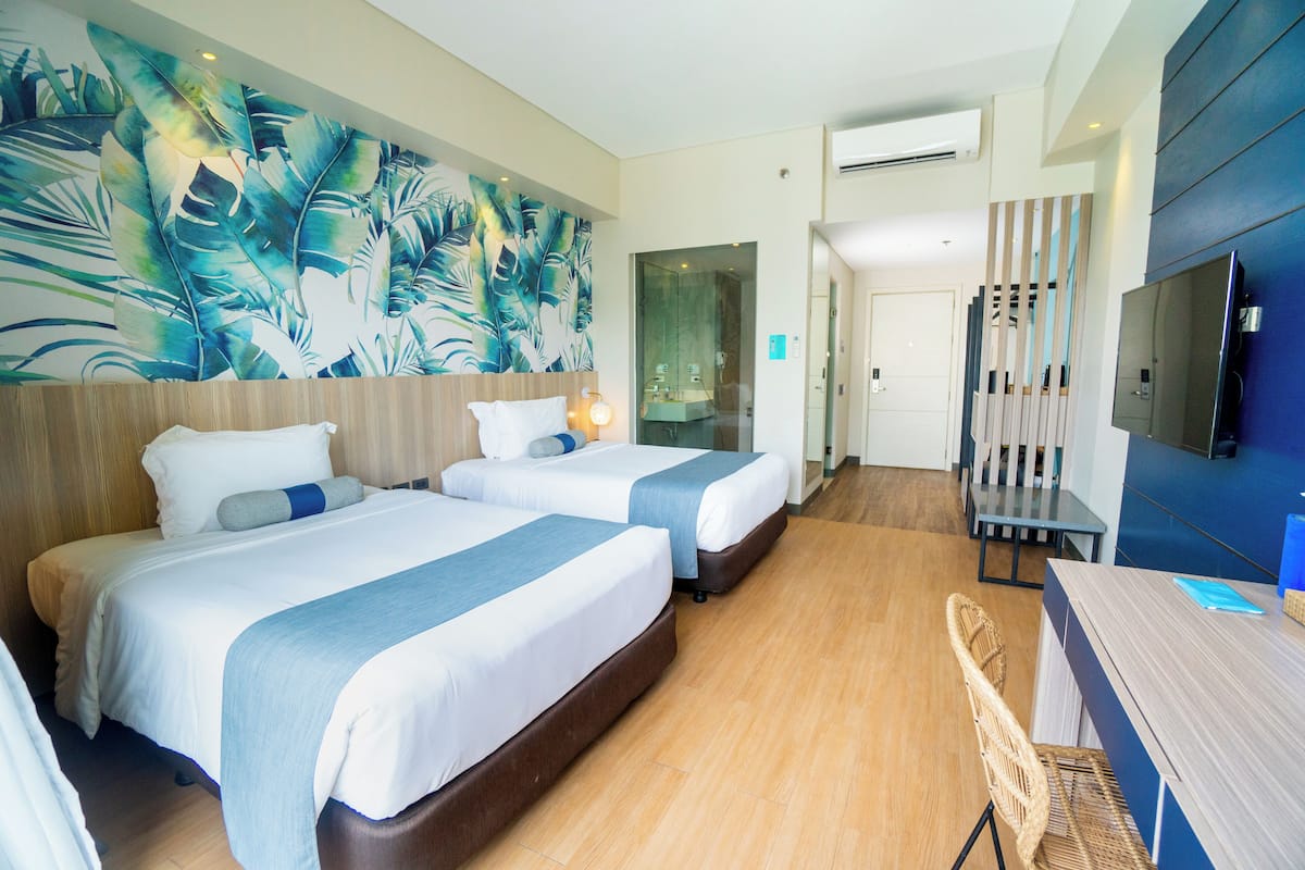Habitación de hotel con dos camas, un mural grande en la pared, un televisor y un escritorio con una silla.