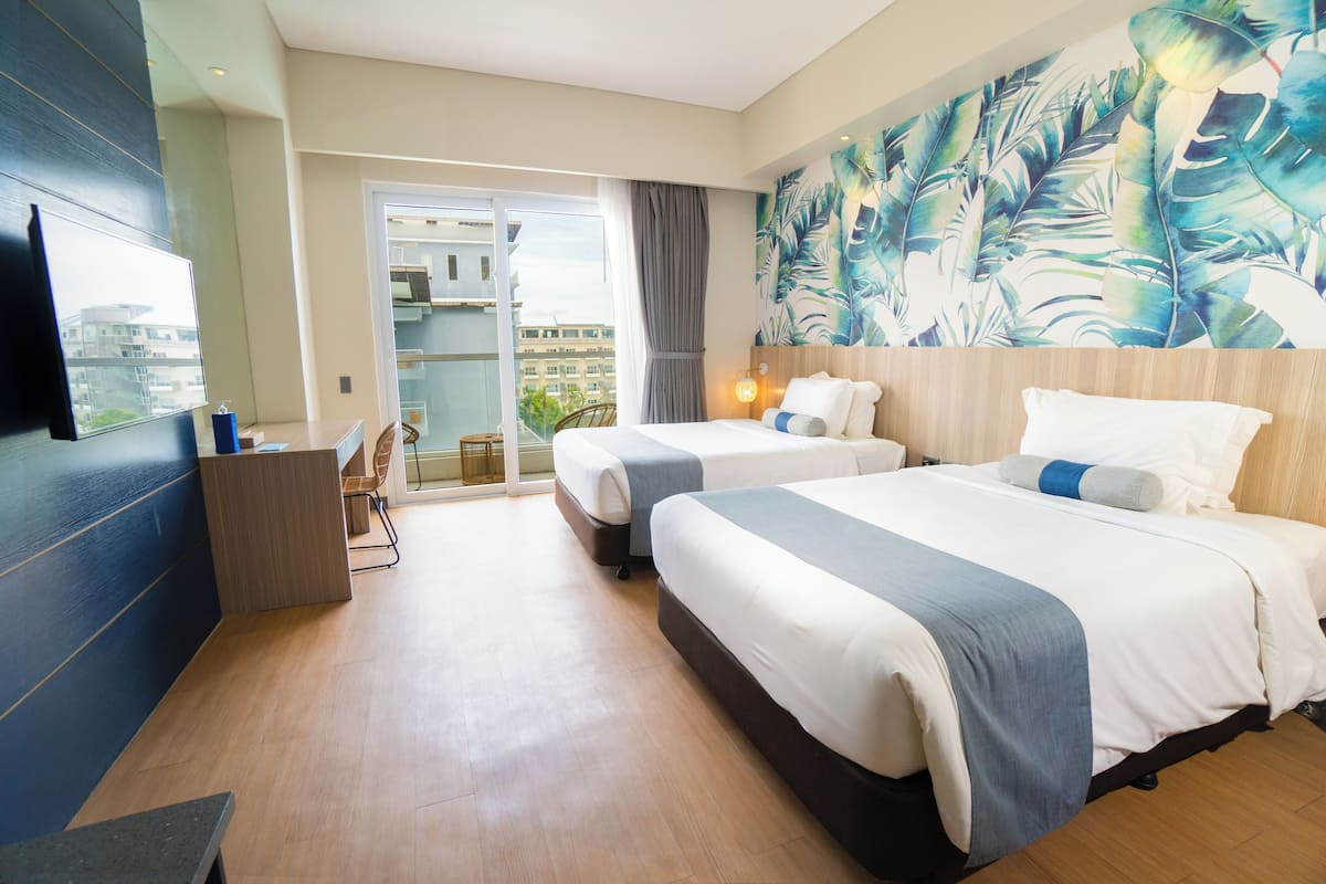 A hotel room with two beds, a desk, and a large window with a view of buildings.