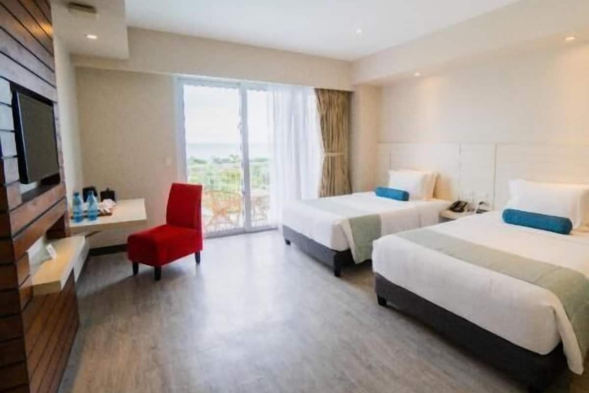A hotel room with two beds, a TV, a red chair, and a view of the outdoors.
